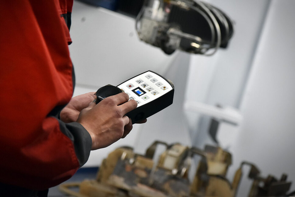 A close-up of an employee's hands holding a remote control to operate a laser cutting machine. The remote control features several buttons and a display, which are used for precise operation of the machine.