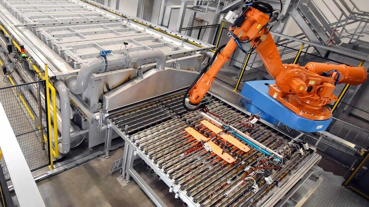 Robotic arm in an automated hot stamping production facility, transferring red-hot metal parts from the furnace to the press.