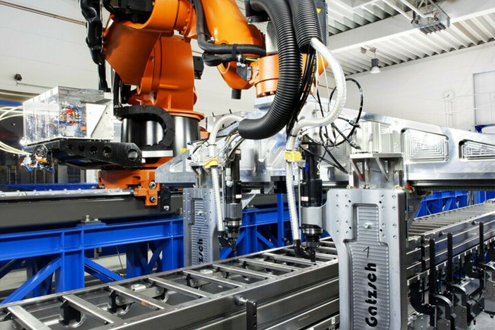 Ein moderner Industrieroboter in einer Produktionshalle, der an einer automatisierten Fertigungslinie arbeitet. Der Roboter führt Nieten und Clinchen durch, um Metallkomponenten präzise zu verbinden. Die Anlage ist an einer Förderanlage befestigt und befindet sich in einer hellen, industriellen Umgebung, die für effiziente und präzise Prozesse in der Fügetechnik steht.