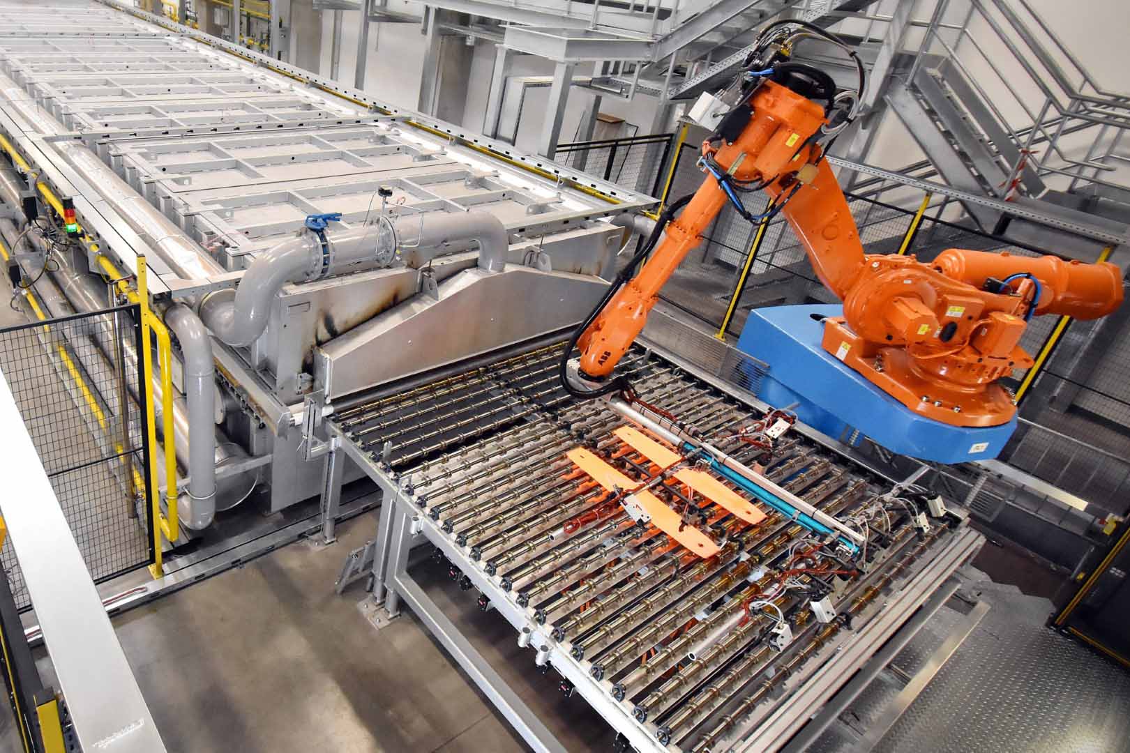 Robotic arm in an automated hot stamping production facility, transferring red-hot metal parts from the furnace to the press.